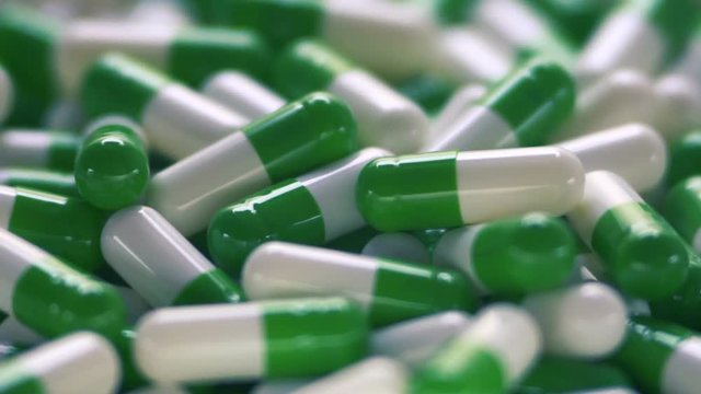 Medical multicolored pills fall on the capsule tablets. White green pills rotate. Pharmaceutical industry. Slow motion. Close-up.