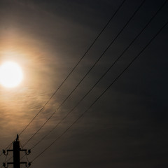 Silhouette of electric wires against the evening sun at sunset in the soft cloudy sky
