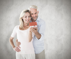 Happy couple holding miniature model house against weathered surface 