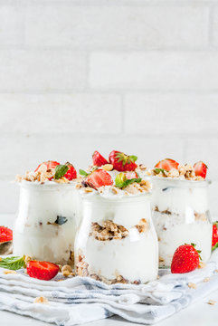 Healthy summer breakfast idea, homemade layered parfe dessert in small jar with granola, yoghurt and strawberry, dark background copy space