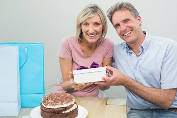 Man giving a happy woman a birthday gift beside cake