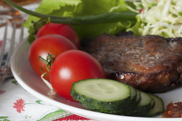 Pork meat grilled with a garnish of fresh vegetables on a white plate