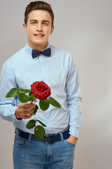 elegant man in a shirt and jeans holds a red rose in his hand