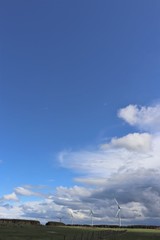 Fototapeta na wymiar Wind tturbines against blue sky with fluffy white clouds