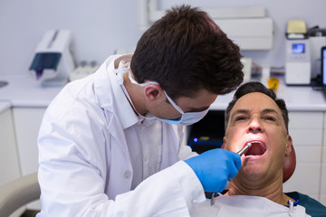 Dentist examining a male patient with tools