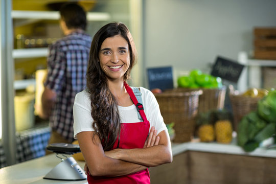 Smiling woman vendor standing at the counter in grocery store with arms crossed