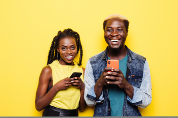 Portrait of an excited young afro american couple holding mobile phones isolated on yellow background