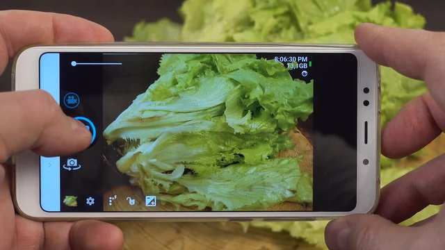 Take a photo on mobile phone of long submarine subway sandwich with fresh lettuce. Wooden background.