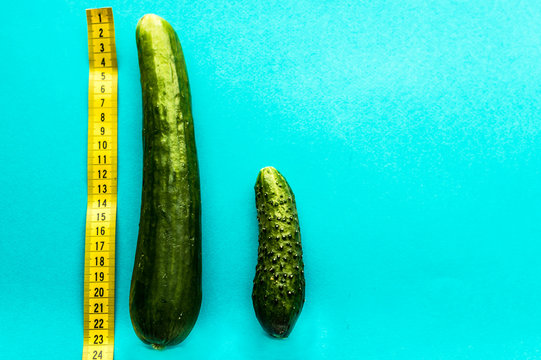 large and small cucumber on a blue background is a rowan with a yellow ruler. concept of a small penis. concept of a large penis