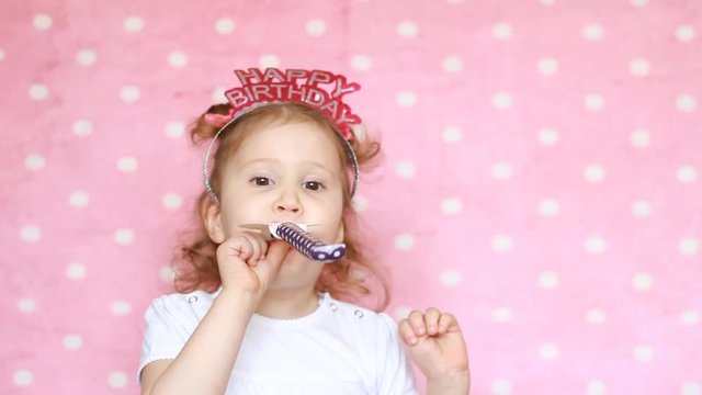 Happy birthday. Party. Celebration. Funny child blowing horn, smiling, have fun, laugh, holidays and celebrate. Close-up portrait cute girl on pink background. Copyspace.