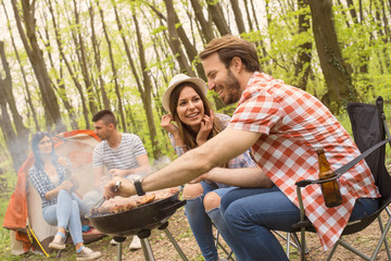 Two couples making barbecue and having fun outdoor while camping together, grill