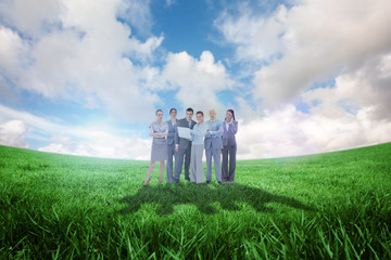 Business team looking at camera against green field under blue sky