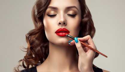 Makeup artist applies  red lipstick  . Beautiful woman face. Hand of make-up master, painting lips...