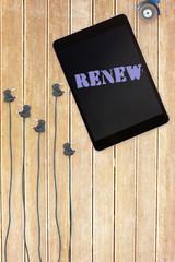 The word renew against tablet and plugs on wooden background