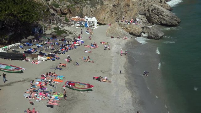 Sunbathing on Playa Calahonda beach below the cliffs and town of Nerja on the Costa del Sol in Spain.