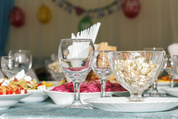 Served banquet table with blurred background. Empty wine glasses, vegetables salad and sliced fruit. Side view