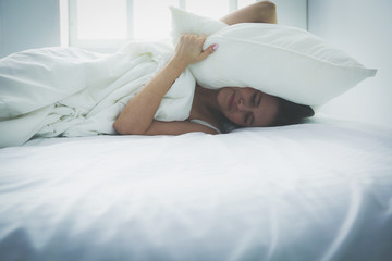 Young caucasian woman covering her head and ears with pillows