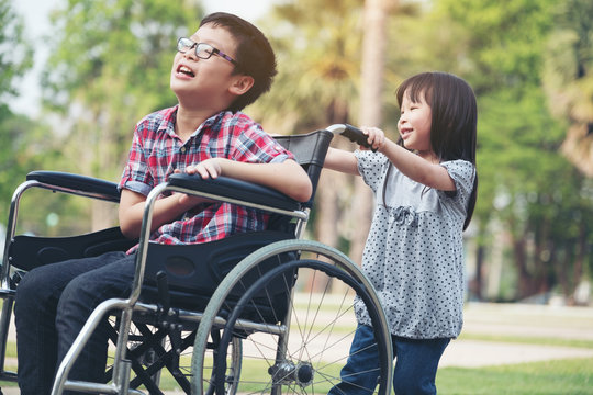 Happy boy in wheelchair with girl try drive a wheelchair of her brother smile, family time