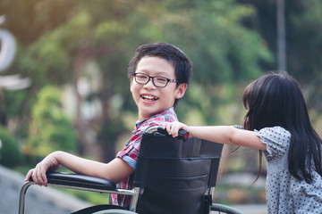 Happy boy in wheelchair with girl try drive a wheelchair of her brother smile, family time