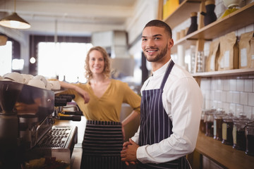 Fototapeta na wymiar Portrait of smiling young waiter and waitress standing by espresso maker