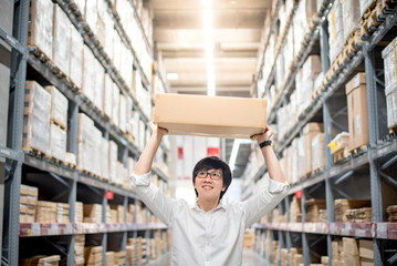 Young Asian man carry paper box over head between row of shelves in warehouse, shopping warehousing or working pick and packing concepts