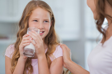 Cute girl drinking milk as she looks to her mother