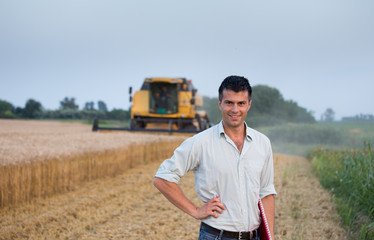 Engineer with notebook and combine harvester in field