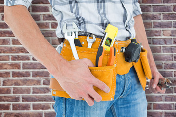 Cropped image of technician with tool belt around waist against red brick wall