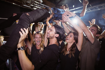 Cheerful fans lifting male performer at nightclub