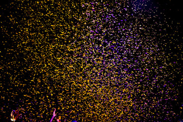 Hundreds of confetti fired on air during a festival at night. Image ideal for backgrounds.  tonality. People with the hands to the sky