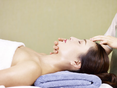 young asian woman receiving face massage in spa salon