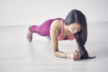 Fototapeta na wymiar Perfect plank. Full-length side view of young beautiful woman in sportswear doing plank while standing in front of window at gym
