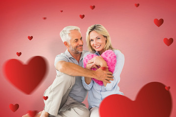 Happy couple sitting and holding heart pillow against red vignette