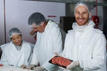 Mid section of butcher holding raw meat patties arranged in tray