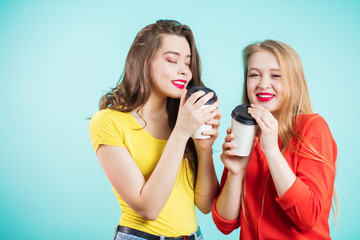 Two smiling girls have coffee time on blue background