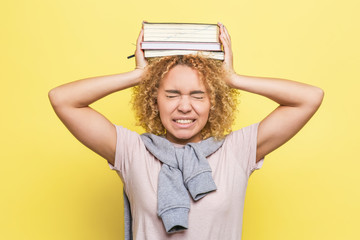 Girl is holding heavy books on her hands. It is painful. She is suffering. Isolated on yellow background.