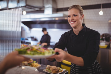 Attractive young female chef giving fresh Greek salad to waiter