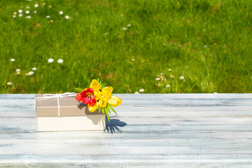 Gift box and flowers on rustic bright table with natural green background. Card concept. Outdoor.