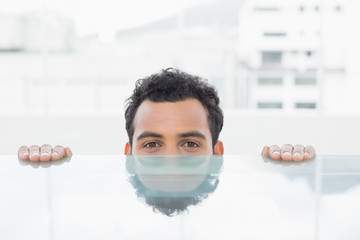 Businessman peeking behind the desk at office