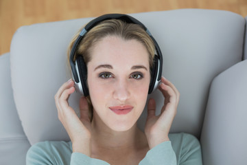 Beautiful casual woman listening with headphones to music lying on couch
