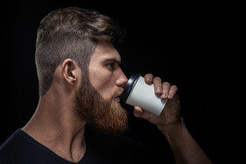 Close up studio shot of side view of young bearded man drinking coffee Coffee on the go studio shot...