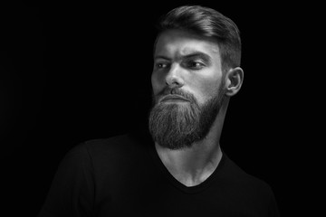 Portrait of handsome single bearded young man with serious expression looking over black background with copy space