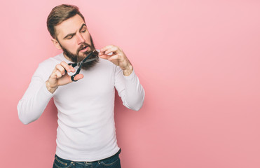 A picture of guy that cuts his beard with the scissors. He is doing that very accurate. Isolated on pink background.