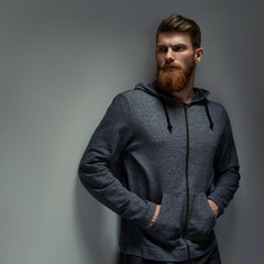 Obraz premium Image of single standing in profile young handsome serious bearded man in grey hoodie over grey background with copy space.
