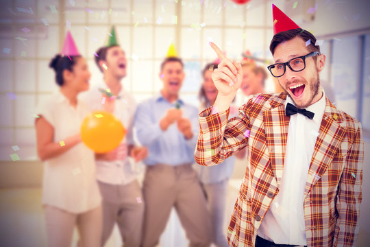 Geeky hipster in party hat pointing against flying colours