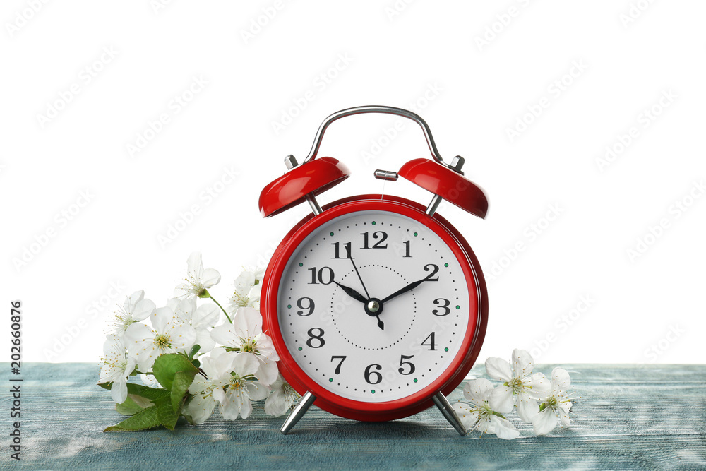 Poster alarm clock and branch with spring blossoms on wooden table against white background. time change co