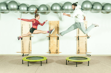 Young beautiful fitness couple workout extreme acrobatic exercise on trampoline jumps as preparation for the competition, selective focus with motion blur