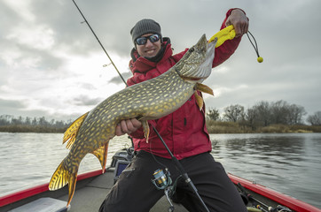 Happy fisherman with big pike fish trophy at the boat with fishing tackles