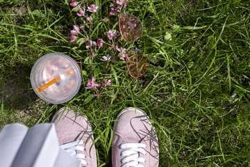 Pink glasses, blooming branch and fresh drink near pink sneakers against a green grass background.