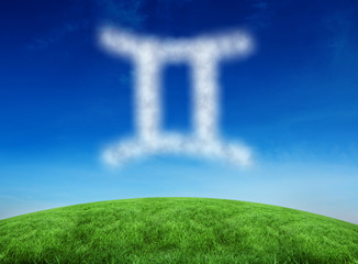 Cloud in shape of gemini star sign against green hill under blue sky